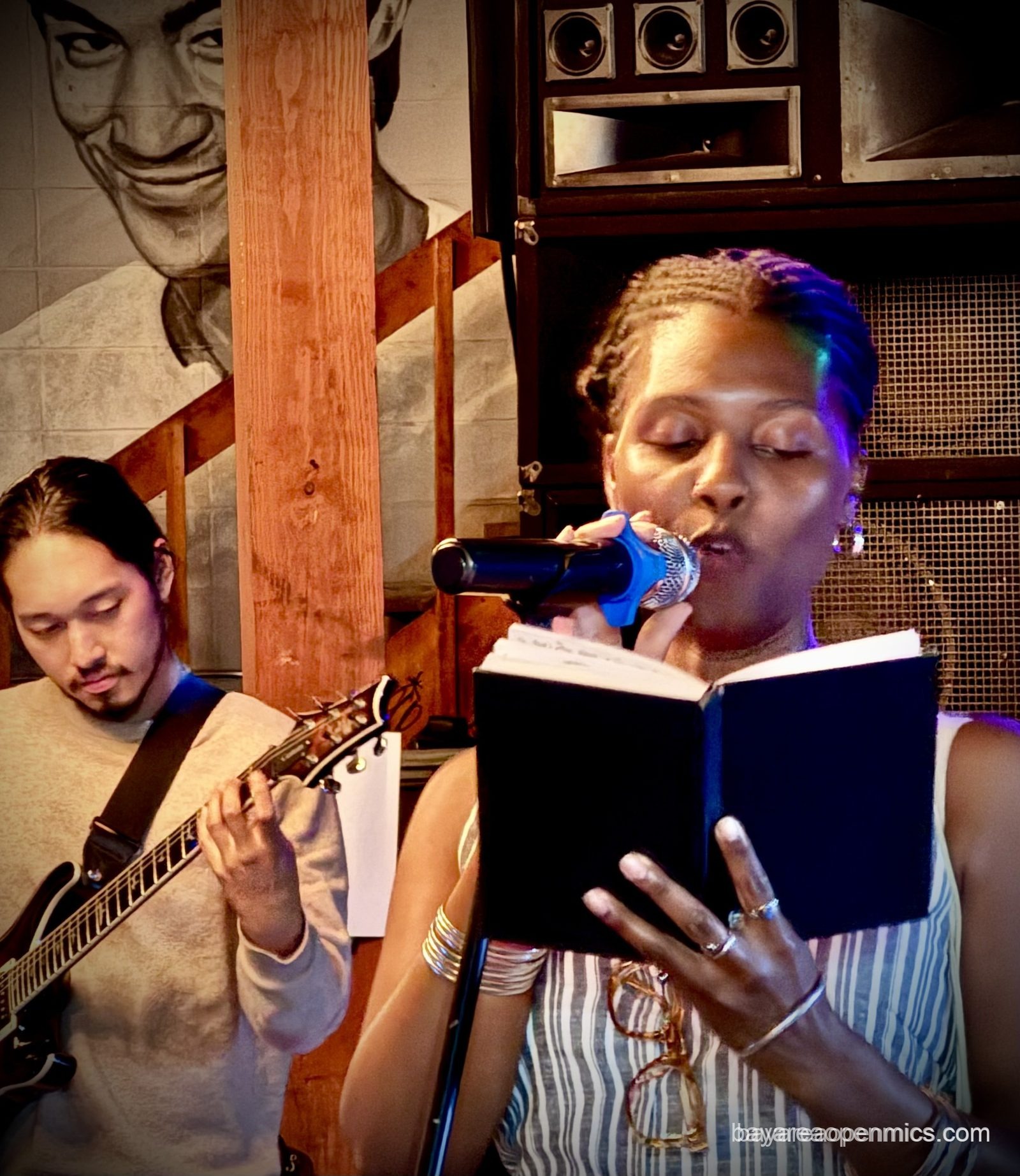 Sabaa Azareena reads poetry from a hardbound book at the Fluid open mic