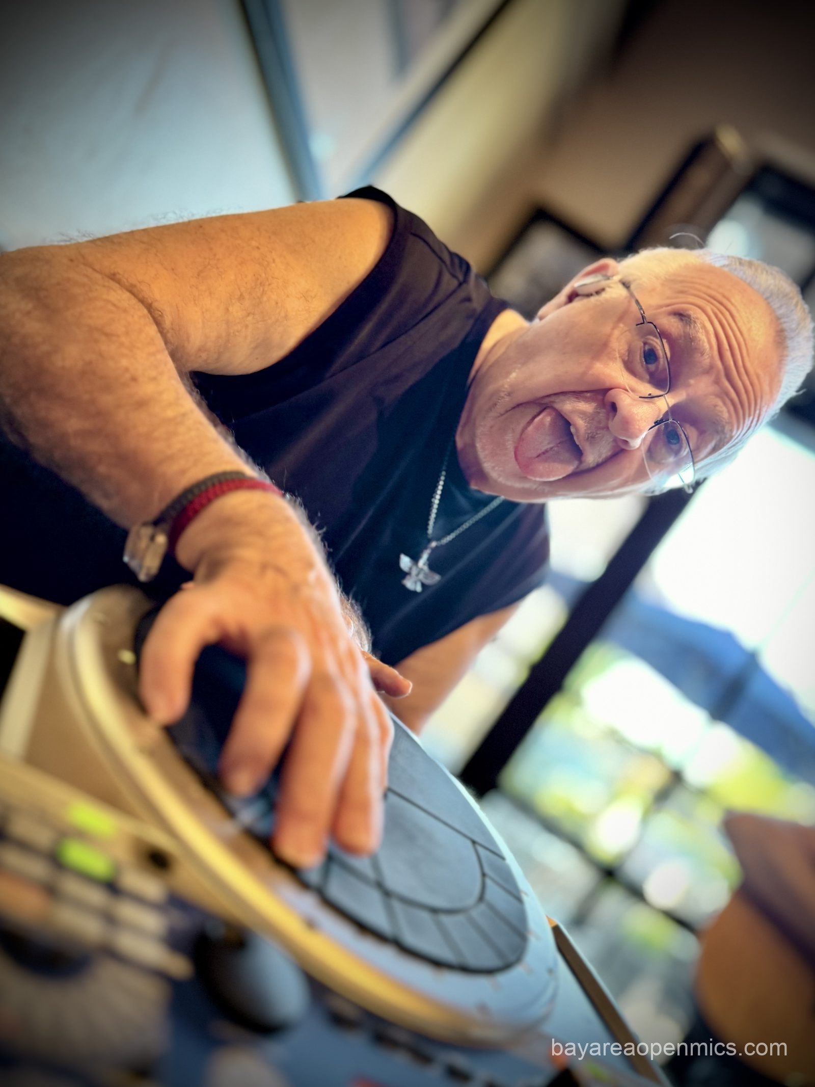 a man sticks his tongue out while splaying his fingers across a circular electronic drum pad