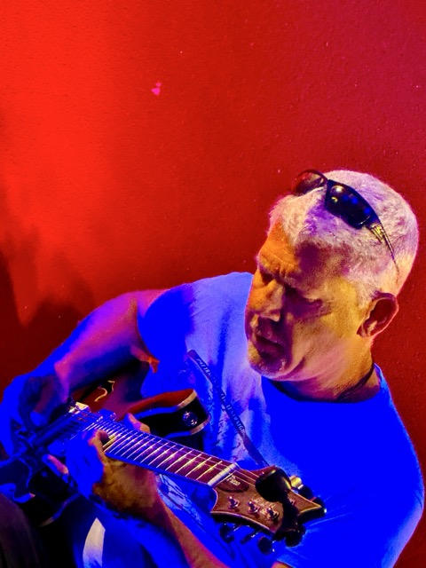 A dramatically colored photo of a white-haired man with sunglasses perched atop his head scowls in concentration while jamming at Pinot's Palette open mic in Livermore