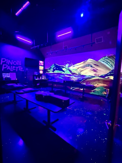 A blacklit storage room at Pinot's Palette casting everything in electric purple and blue