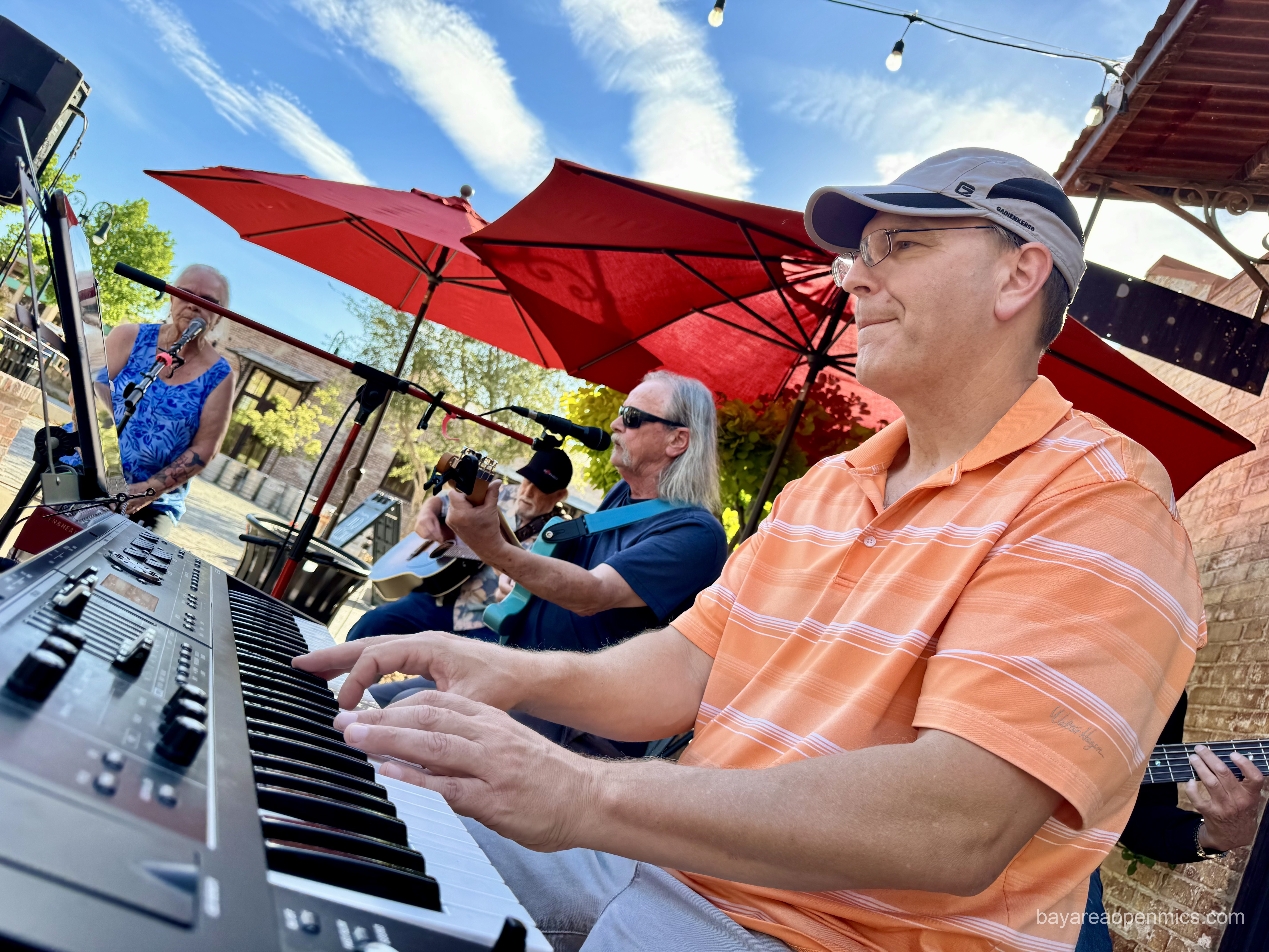 A man in an orange striped shirt plays keyboard in front of other musicians