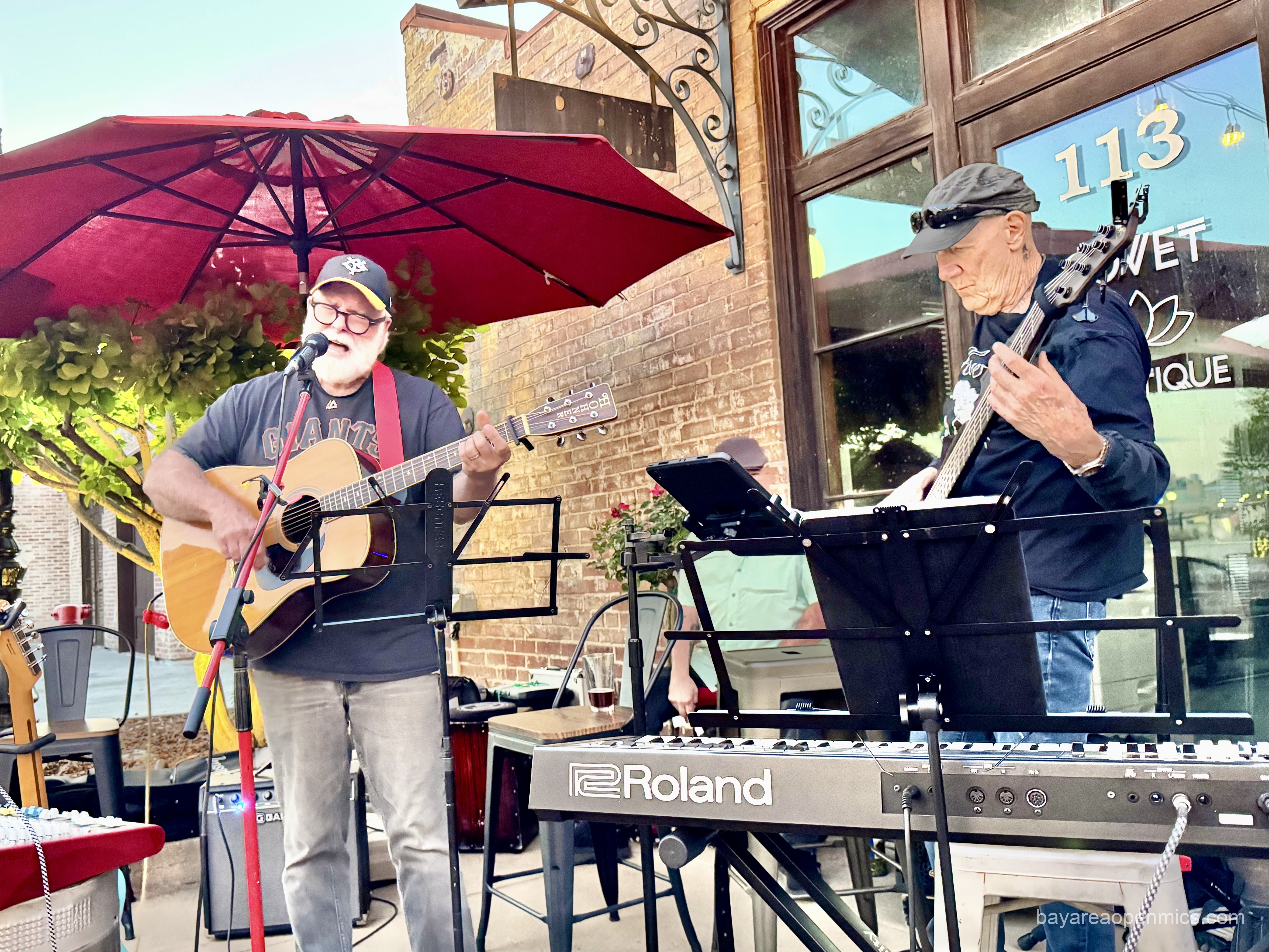 two men play music under a red patio umbrella
