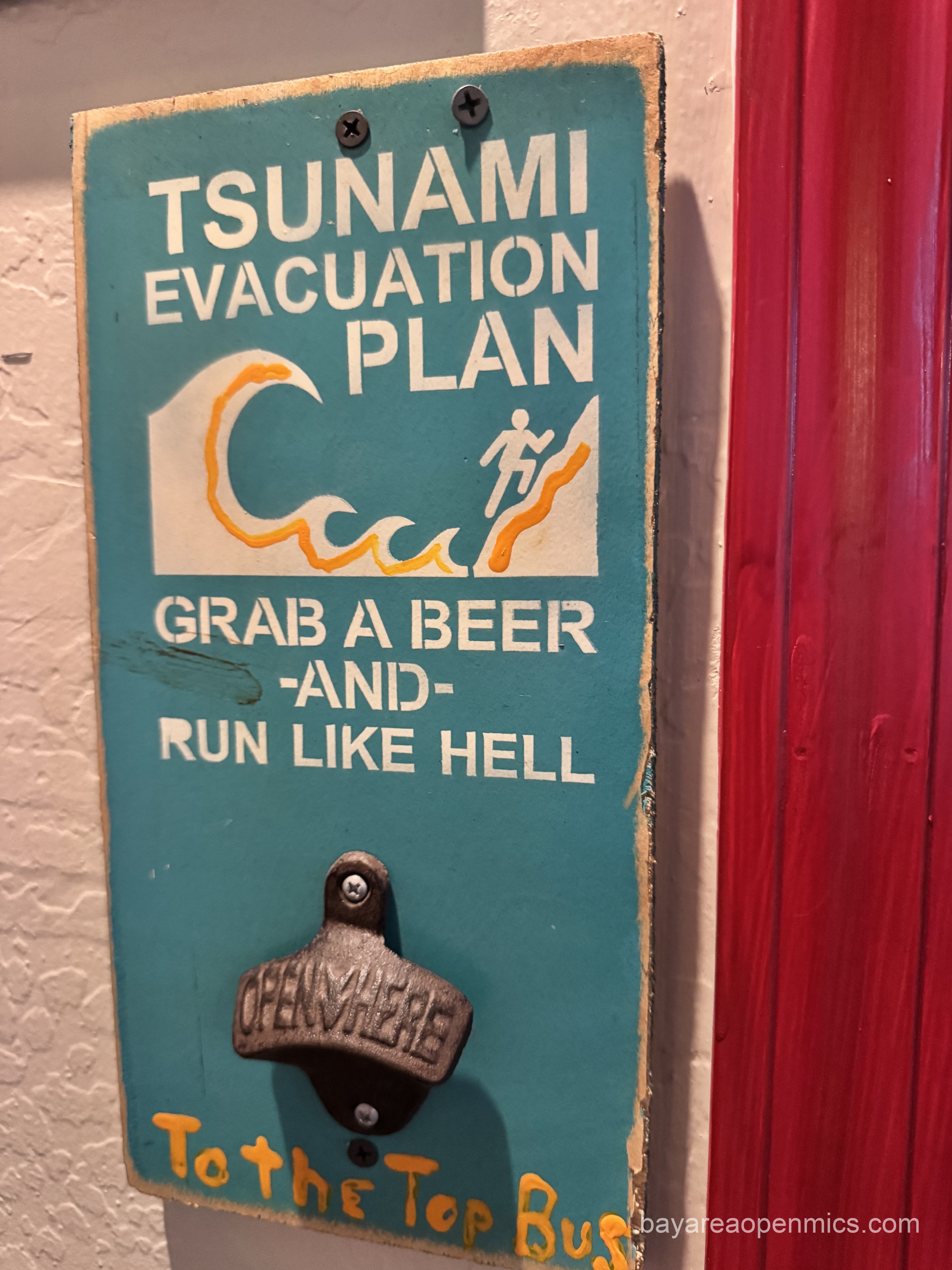 A sign reads Tsunami evacuation plan: grab a beer and run like hell with a bottle opener beneath it