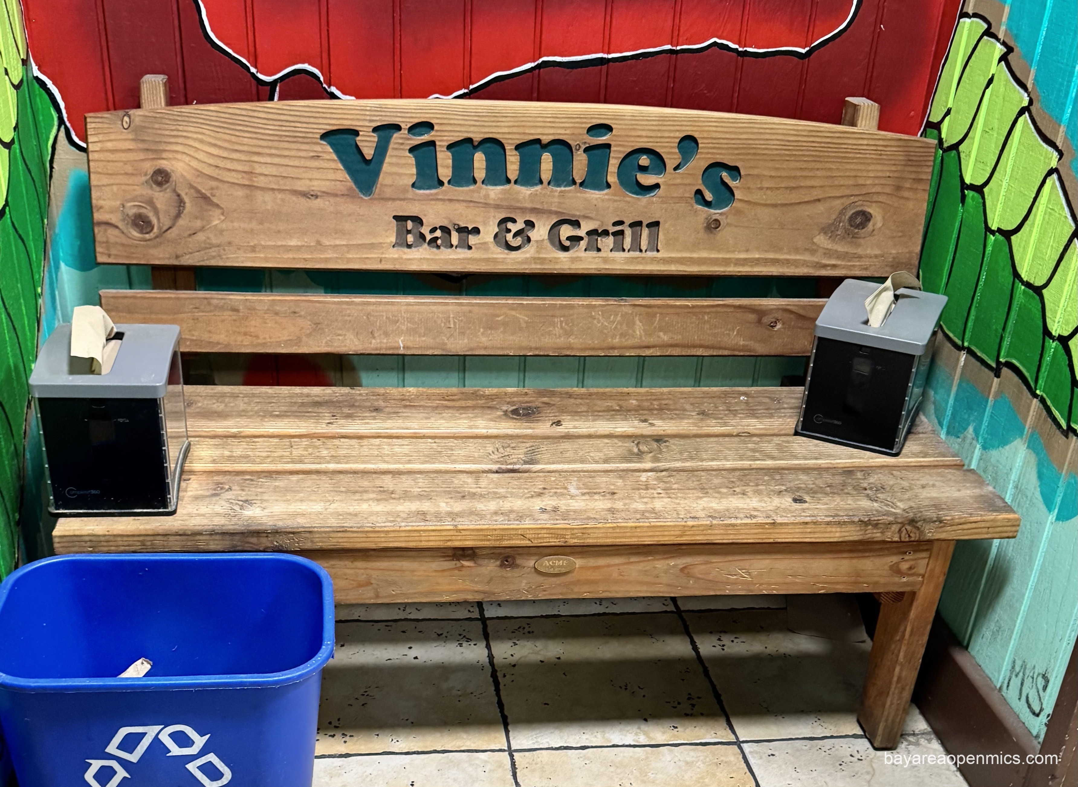 A wooden bench with a 'Vinnie's Bar and Grill' logo hosts two paper towel dispensers at each end