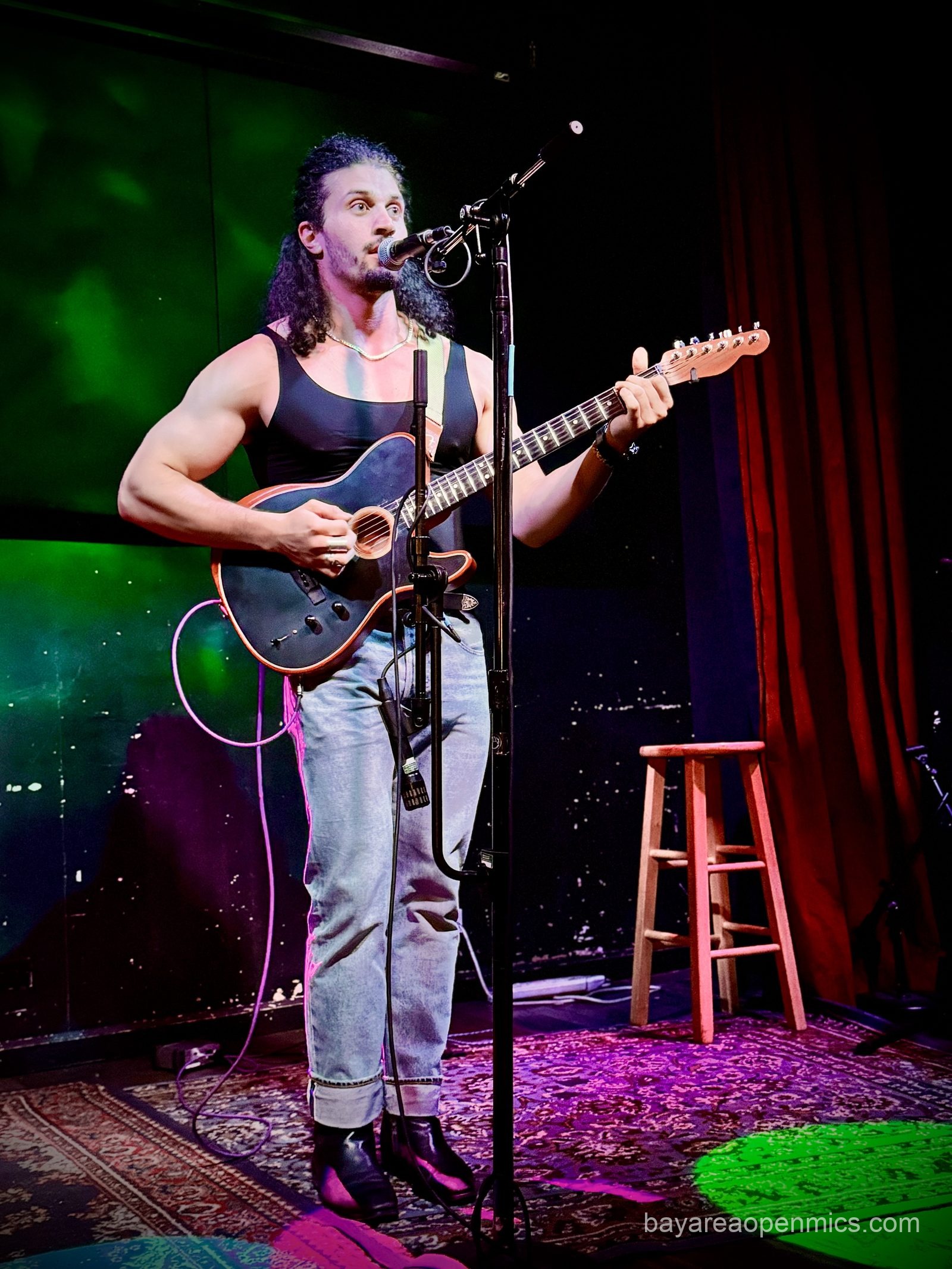 Miguel Love standing with his guitar at the Hotel Utah open mic