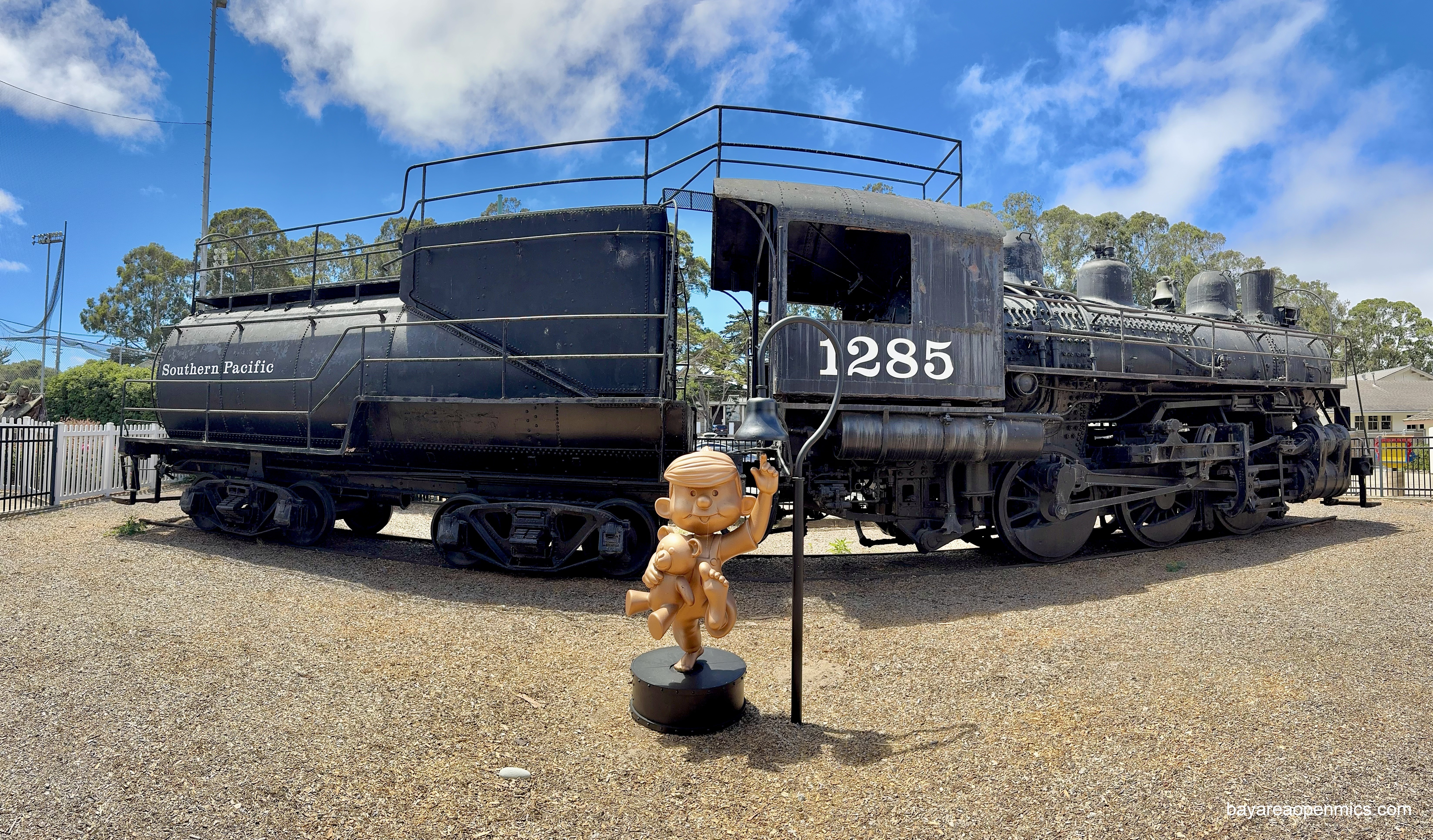 A bronze statue of Dennis the Menace stands in front of a ten-ton locomotive at Dennis the Menace Playground in Monterey.